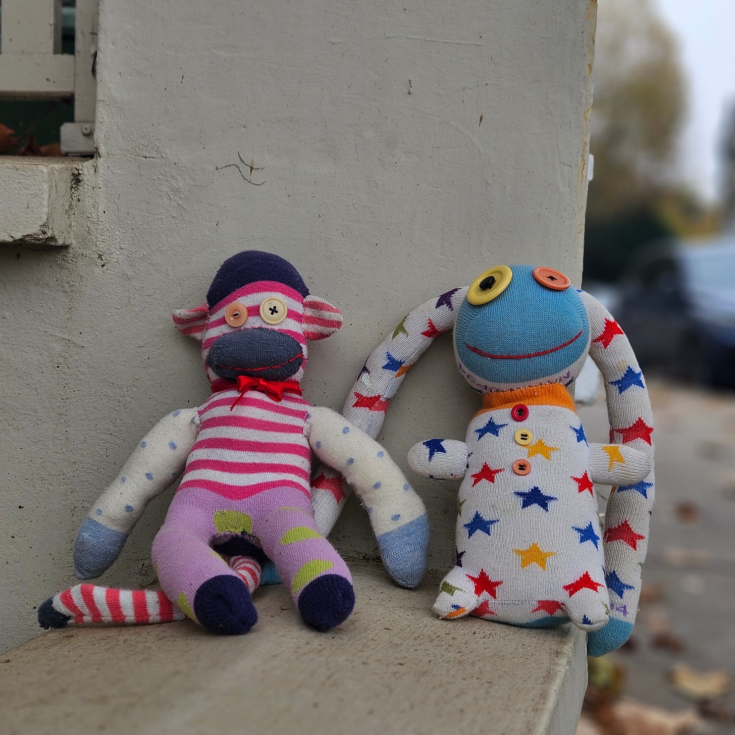 2 colorful stuffed sock puppets on a cement sidewalk railing