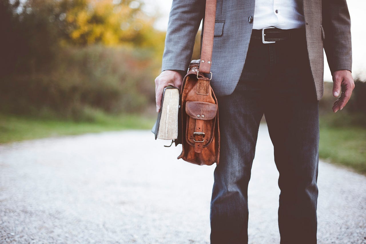 A man walking on a quiet gravel road with a book and briefcase