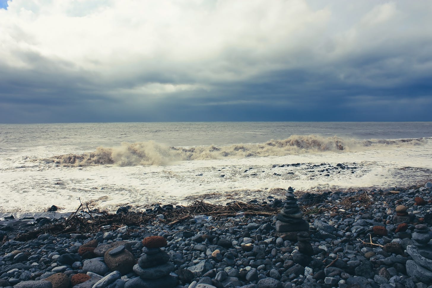 Scenic View of a Pebble Beach with a Rocky Shoreline Barrier and a Stormy Sea in the Background