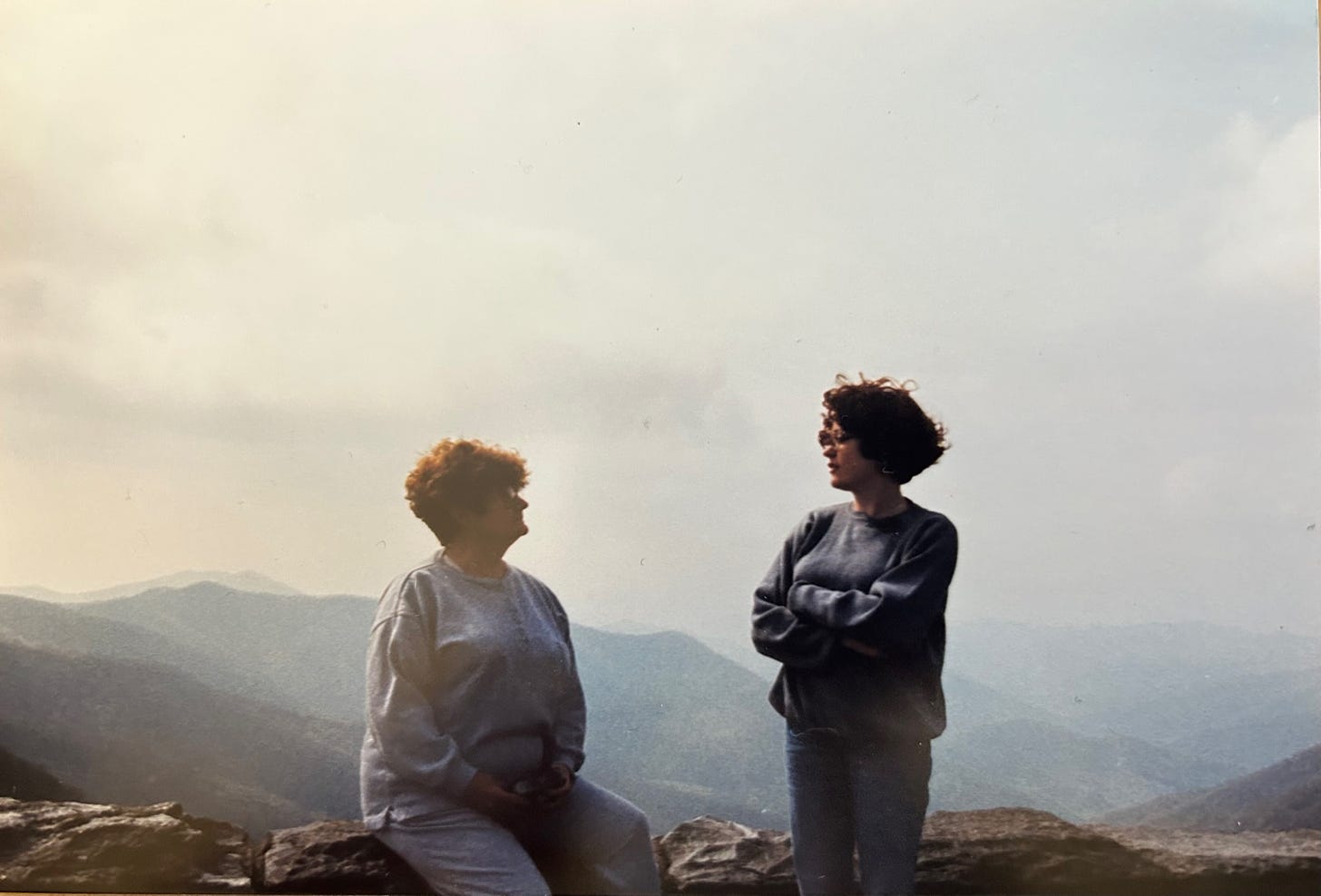 Two women, one older and one younger, both white, both wearing gray sweaters and jeans, in front of the Blue Ridge Mountains