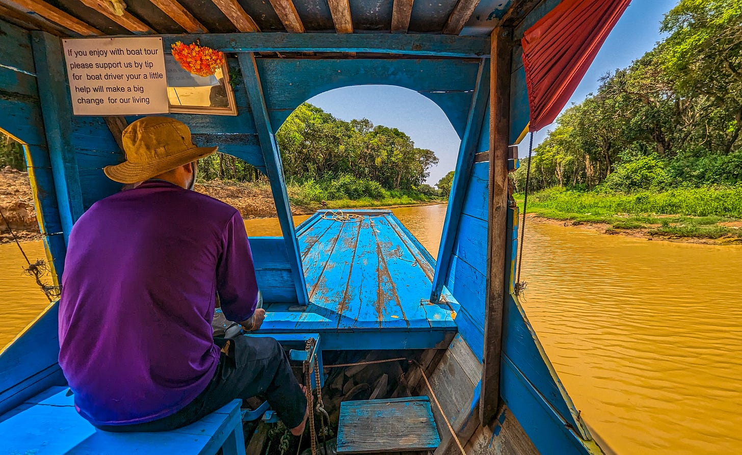 A photo from inside a boat motoring up a narrow muddy channel. Thick stands of tree line the river. 