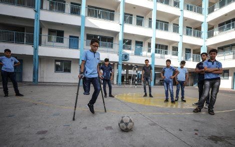 A Palestinian boy missing a leg from the knee down is shown with schoolmates as he attempts to kick a soccer ball.