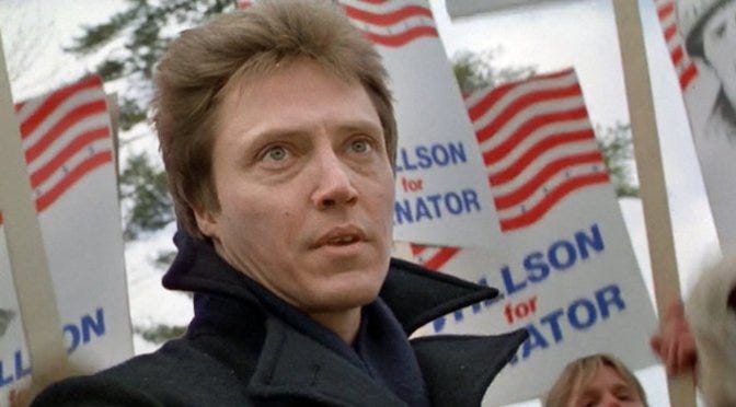 Christopher Walken in The Dead Zone, staring toward the stage at a political rally with Willson for Senator signs held up behind him in the crowd.