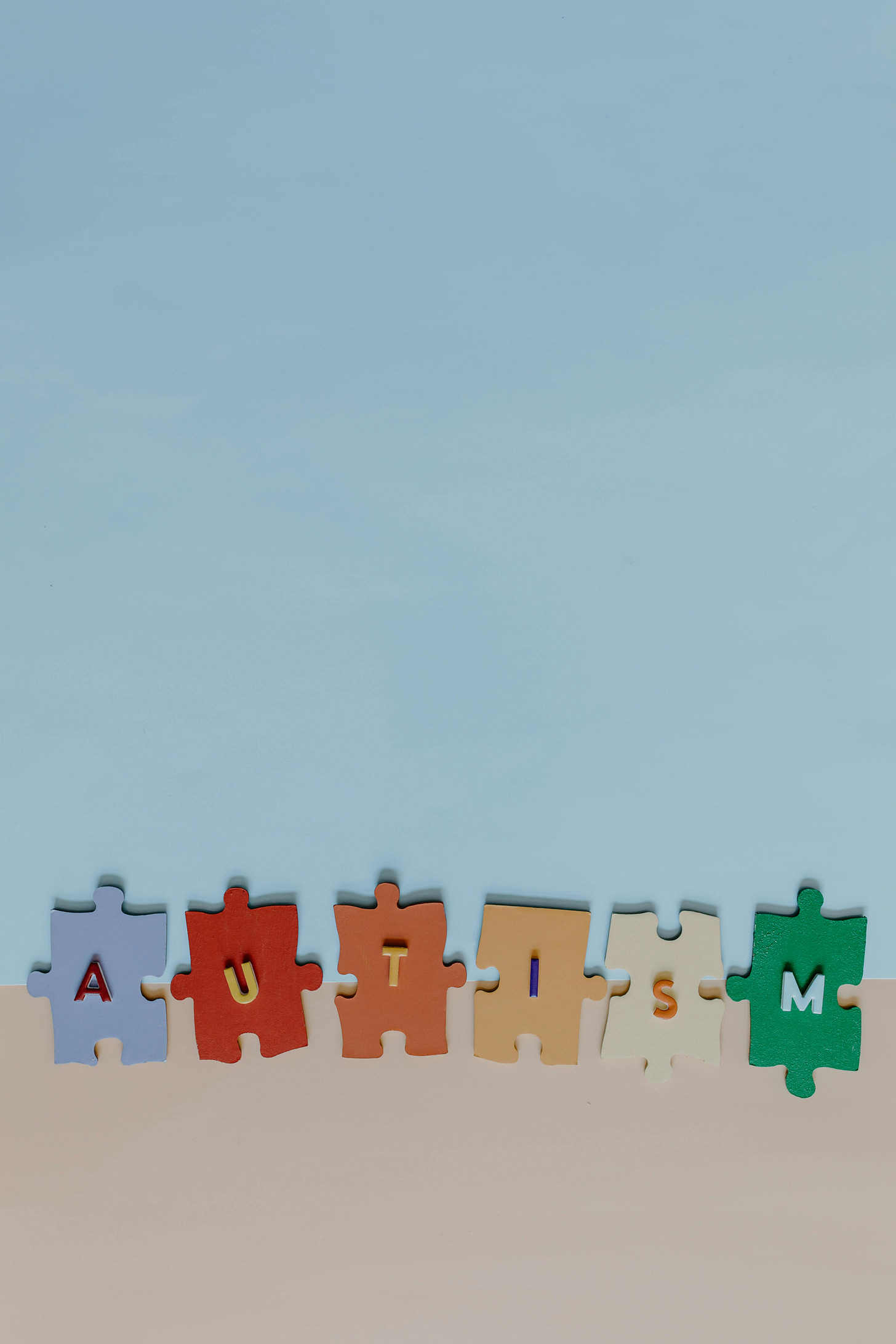 Split Blue and brown background with puzzle pieces in the middle spelling Autism Split Blue and brown background with puzzle pieces in the middle spelling Autism