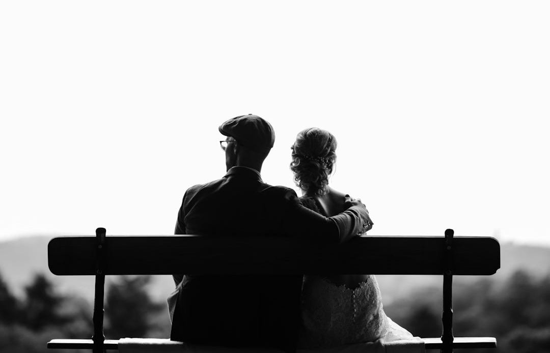 couple sitting on bench under tree grayscale photography couple sitting on bench under tree grayscale photography