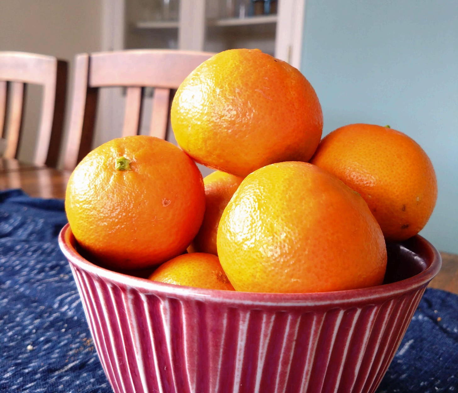 Photo of a red bowl containing 6 bring orange mandarins. 