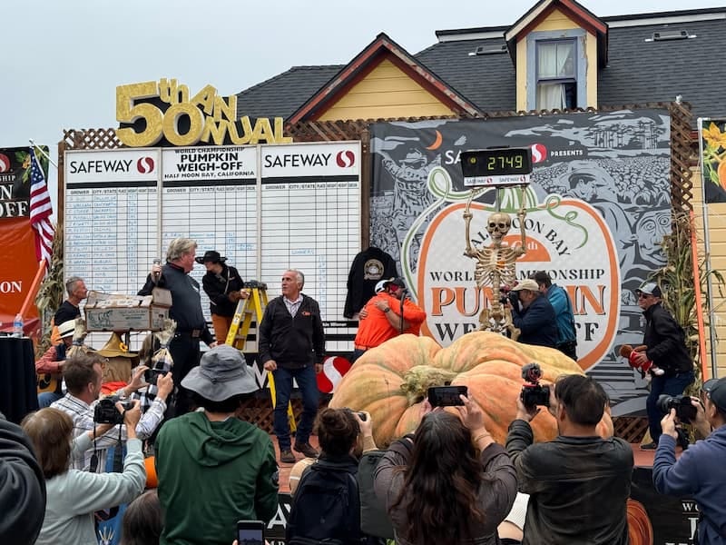 A photograph of the 50th Annual Half Moon Bay Pumpkin Weigh-Off - an enormous pumpkin sits on the scales, 2749 reading out on the display.