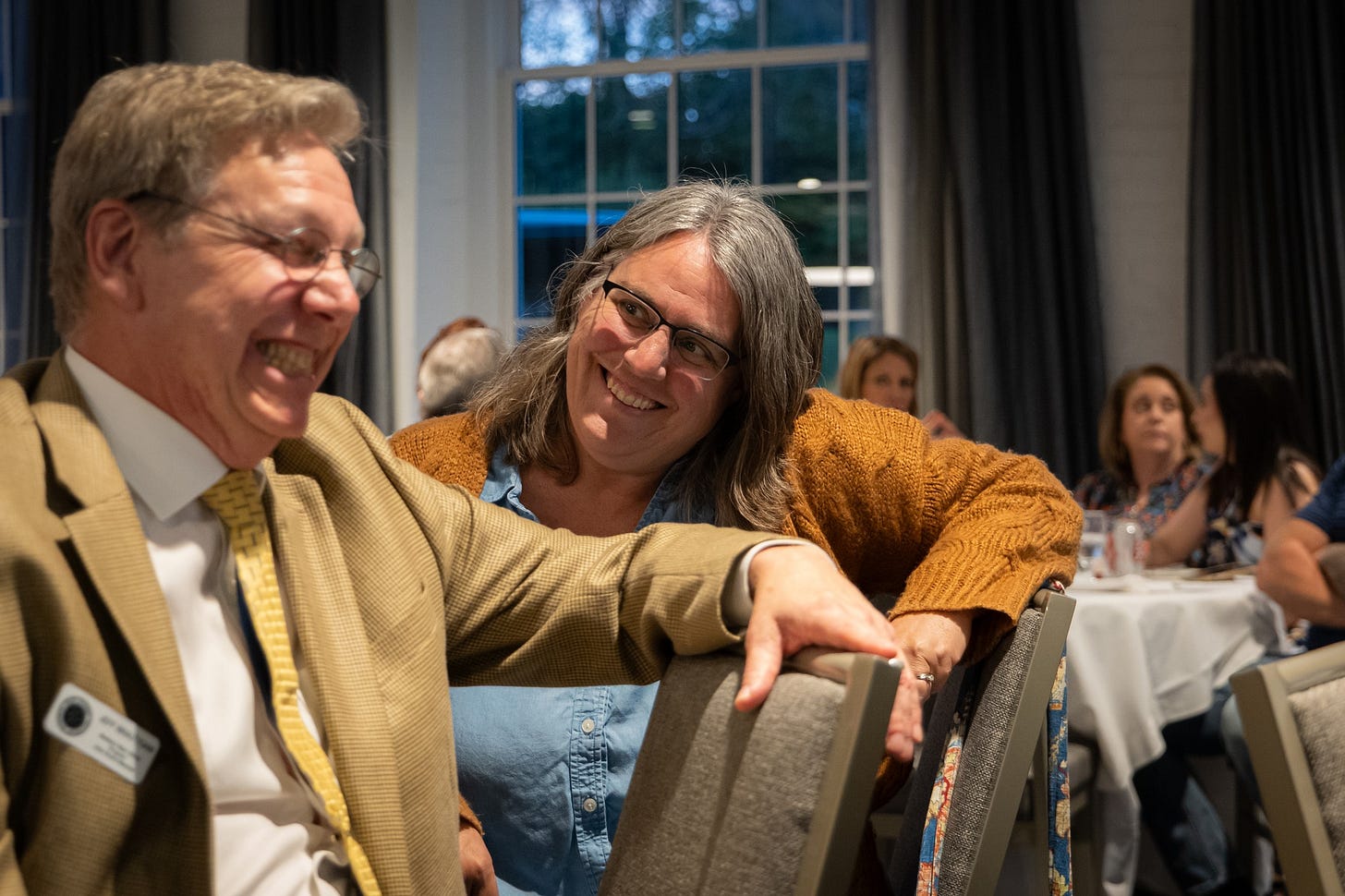 In the foreground, Jeff is making a gritted face look of excitement and behind him, Robyn is smiling and watching him in a snarky kind of way
