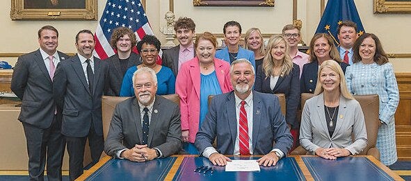 Gov. Eric Holcomb ceremonially signs State Rep. Sharon Negele's (R-Attica) law improving breast cancer screening and prevention for Hoosier women Thursday, Aug. 15, 2024, at the Statehouse in Indianapolis. Bill co-authors State Reps. Brad Barrett (R-Richmond) (seated, left), and Cherrish Pryor (D-Indianapolis) (standing, fourth from left) joined Holcomb (seated, center), State Rep. Lori Goss-Reaves (R-Marion) (standing, fifth from right) and Negele (seated, right). Representatives from Dant Advocacy, Hoosier Breast Cancer Advocacy, Lilly, Indiana University of Medicine, Indiana Commission for Women and Catalyst were also present.