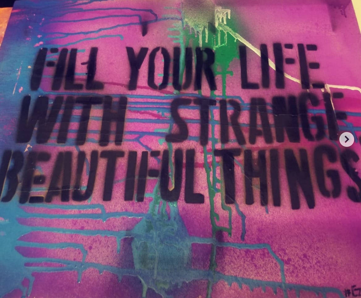 A purple and blue spray painted sign that says "Fill your life with strange and beautiful things"