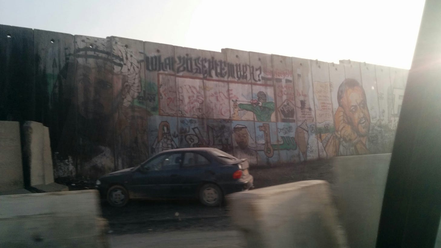 Graffiti covers a large concrete wall bordering a road