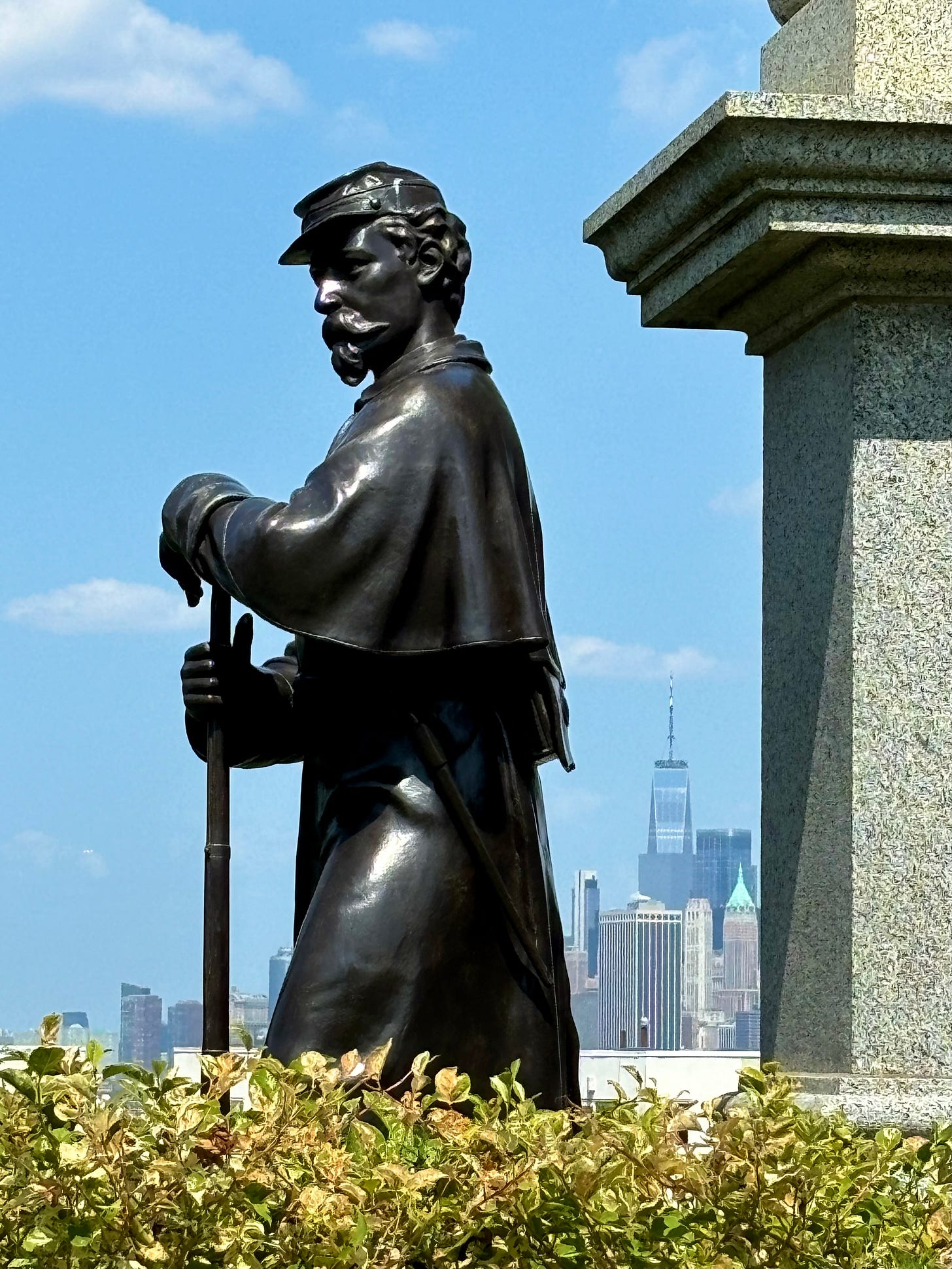 A close up of one of the soldiers from the monument. In the distance, small behind him, is the World Trade Center.