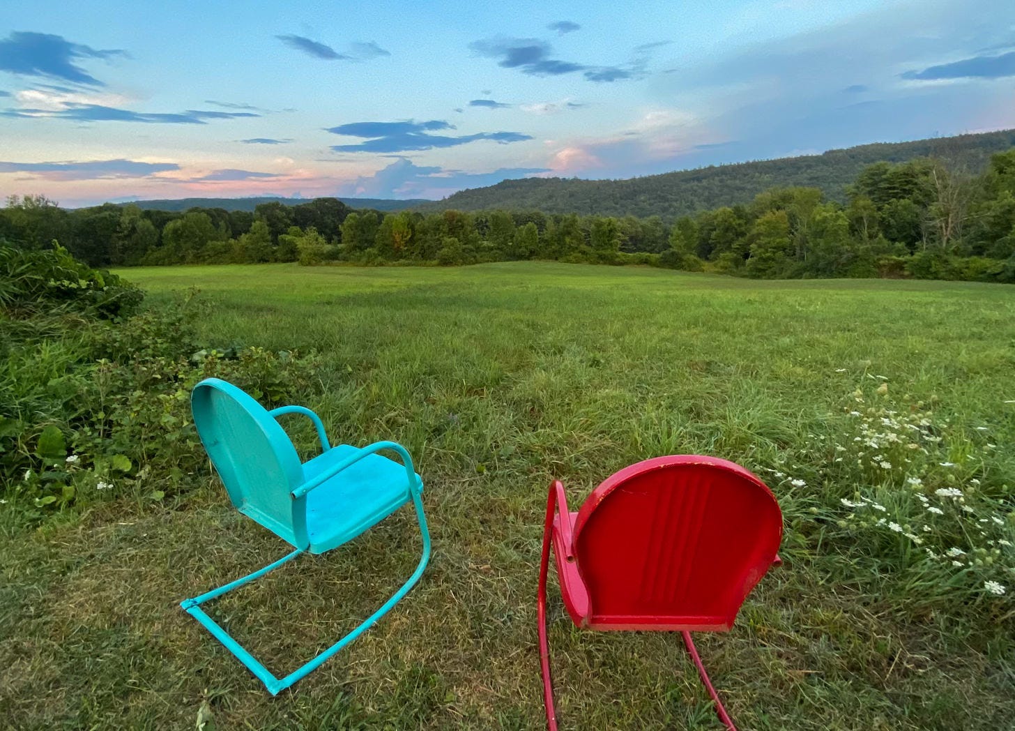 Two 1960's vintage metal chairs red and turquoise facing grassy meadow and hills at dusk