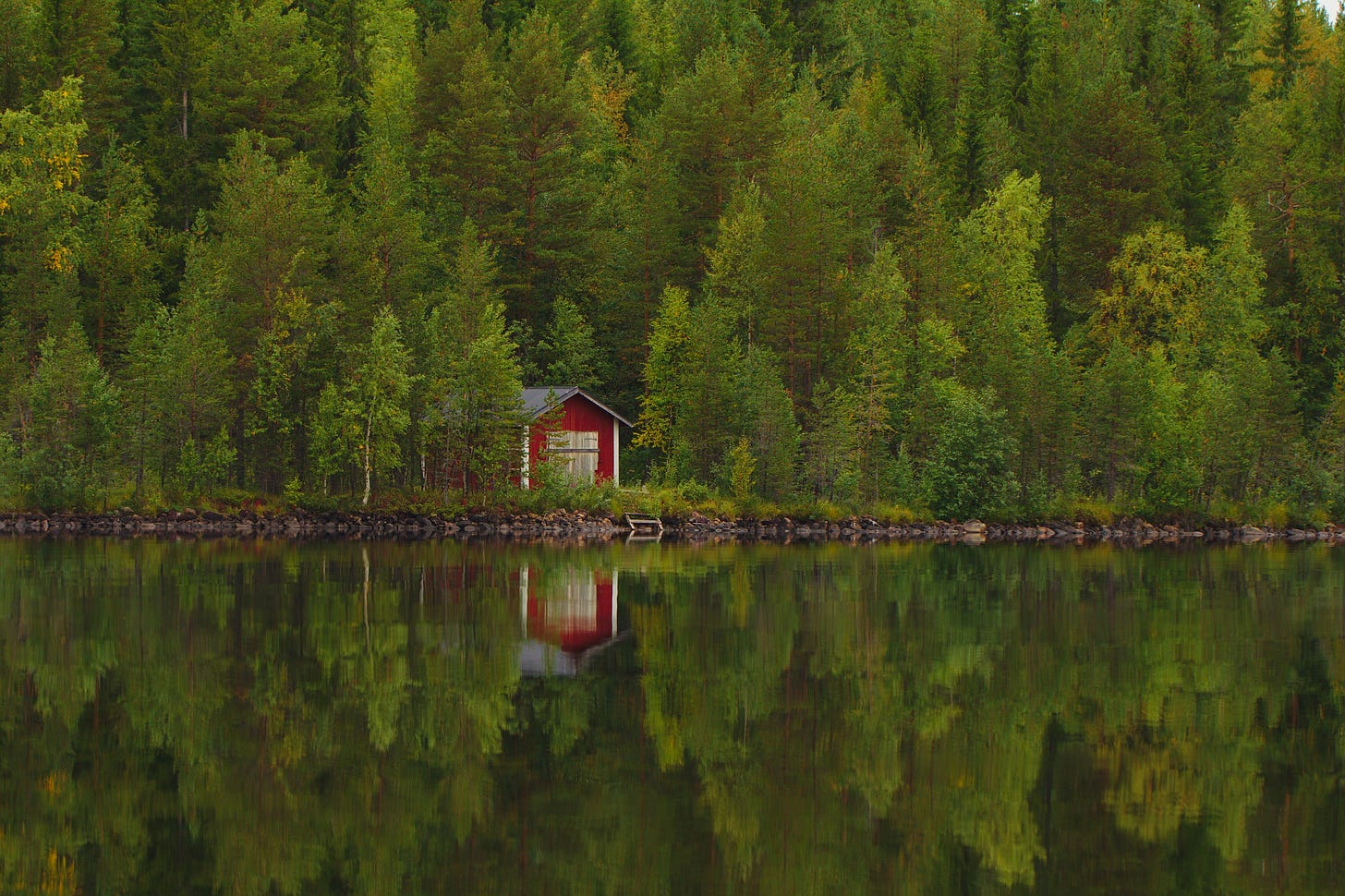 Red hut in a green forest by a lake, Sweden.