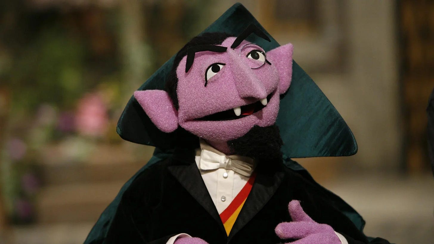Marioneta morada de aspecto intelectual y rasgos vampíricos con túnica y camisa blanca con pajarita