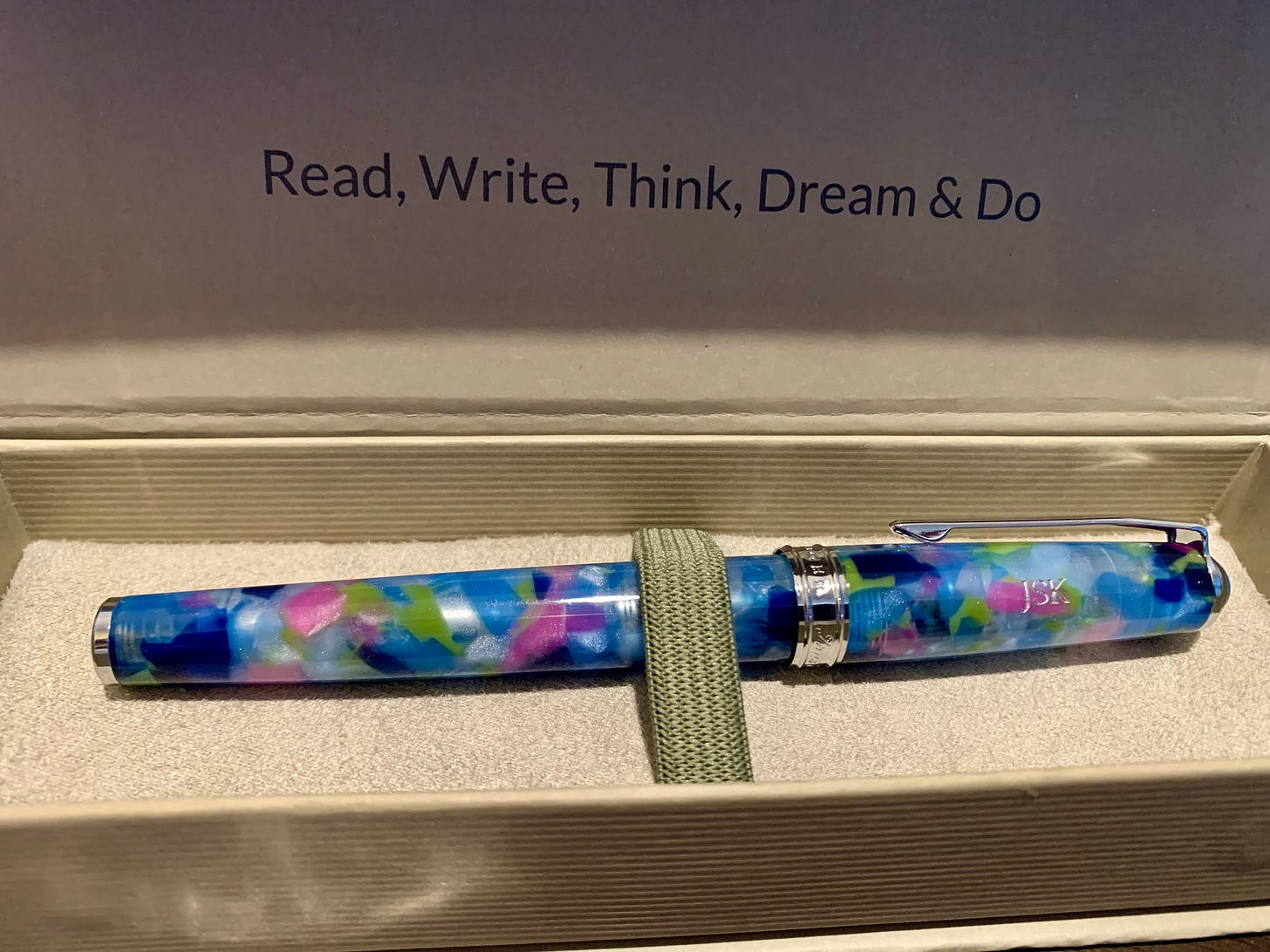 A mottled blue, green, pink, and white pen in a beige case whose inner lid reads "Read, Write, Think, Dream, and Do"
