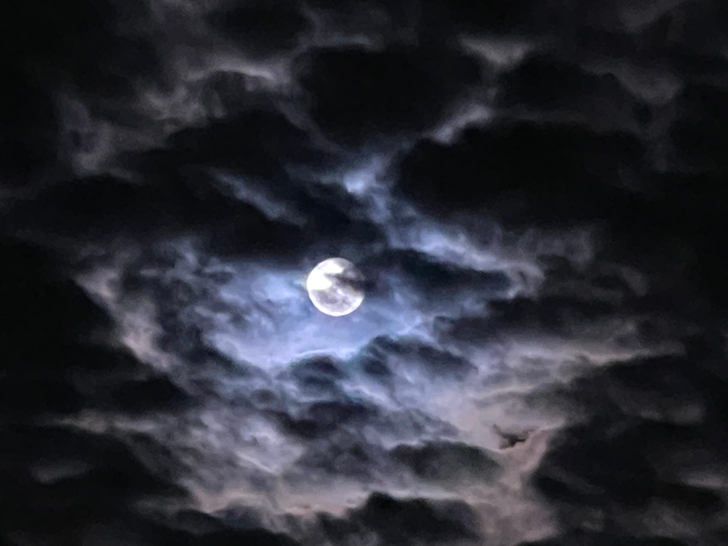 bright shining moon behind wispy grey mottled clouds