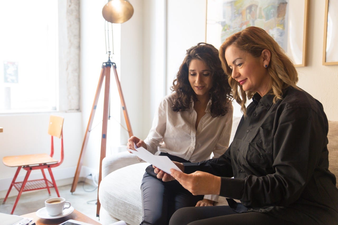 Middle aged woman sitting on couch with young woman giving advice