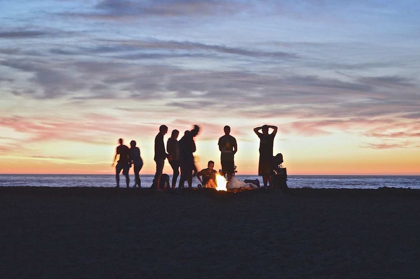 Several people silhouetted around a campfire on the beach at sunset. Several people silhouetted around a campfire on the beach at sunset.
