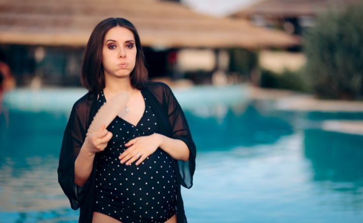 Woman fanning herself by pool during her summer pregnancy
