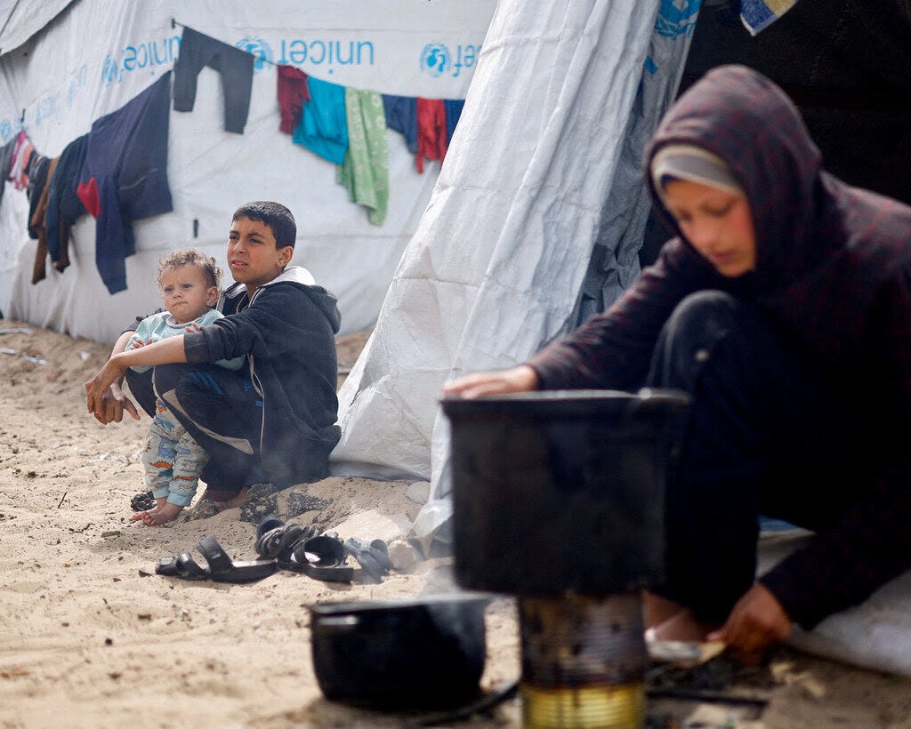 Children sitting on the ground outside white tents. 