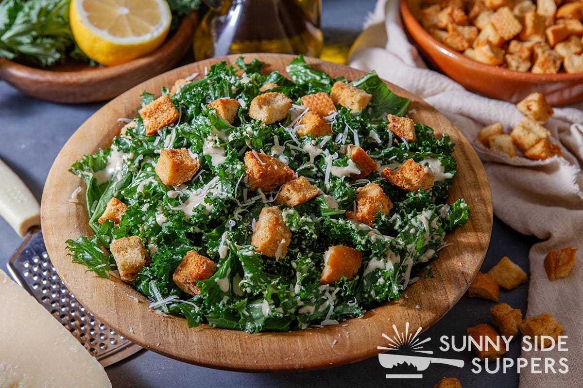 A wooden bowl with kale Caesar salad in it.