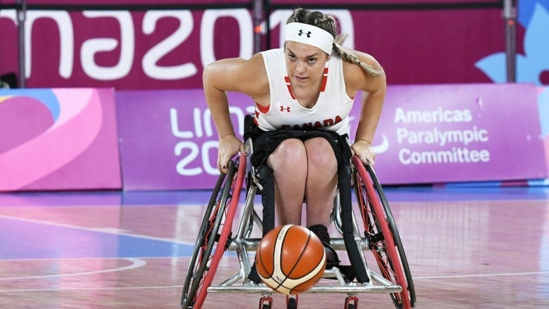 A female wheelchair basketball player moves down the court with the ball.