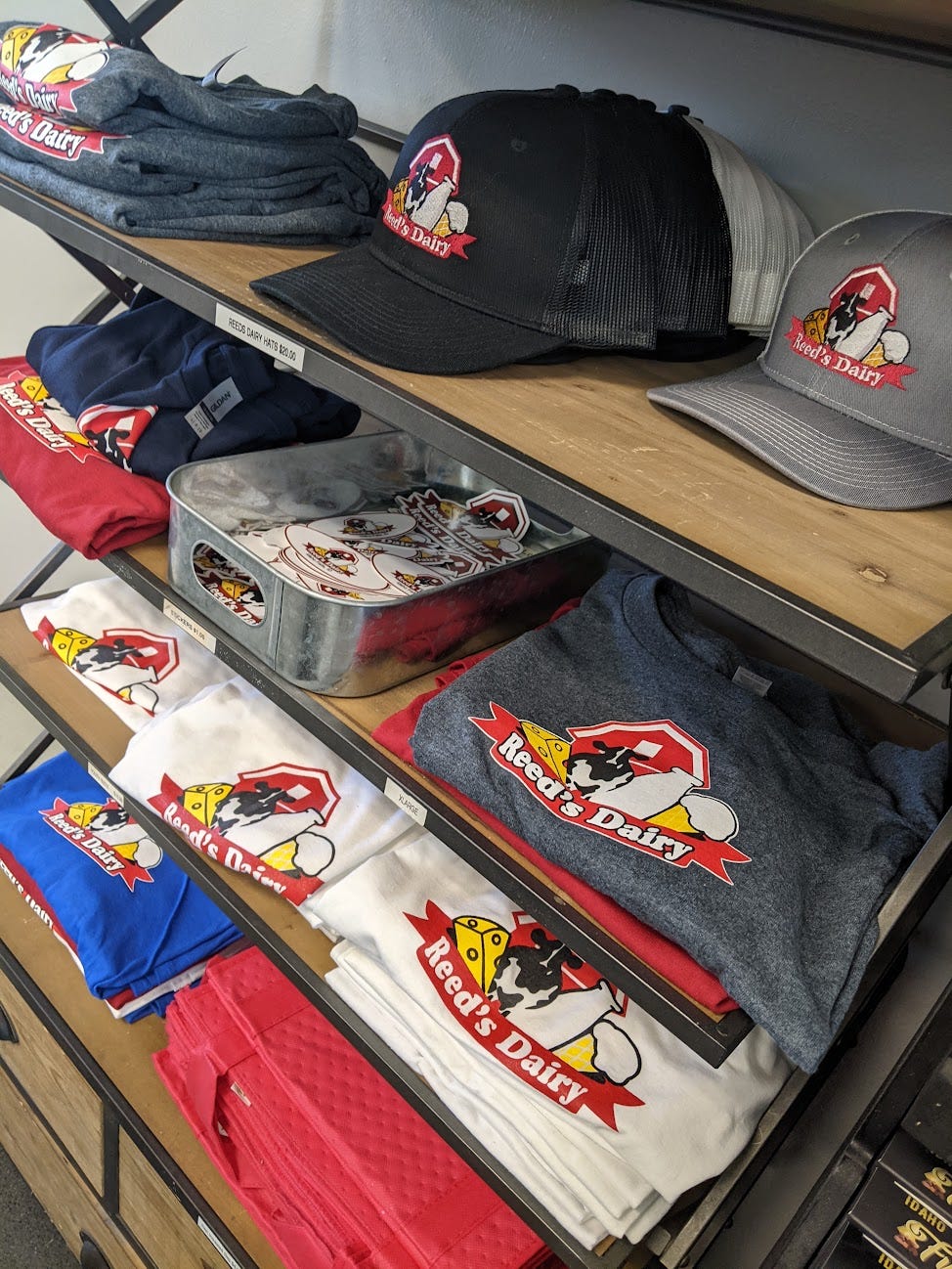 A wall of merchandise--hats, shirts, stickers, etc., all with the Reed's Dairy logo of a red barn, a cow, and assorted dairy products