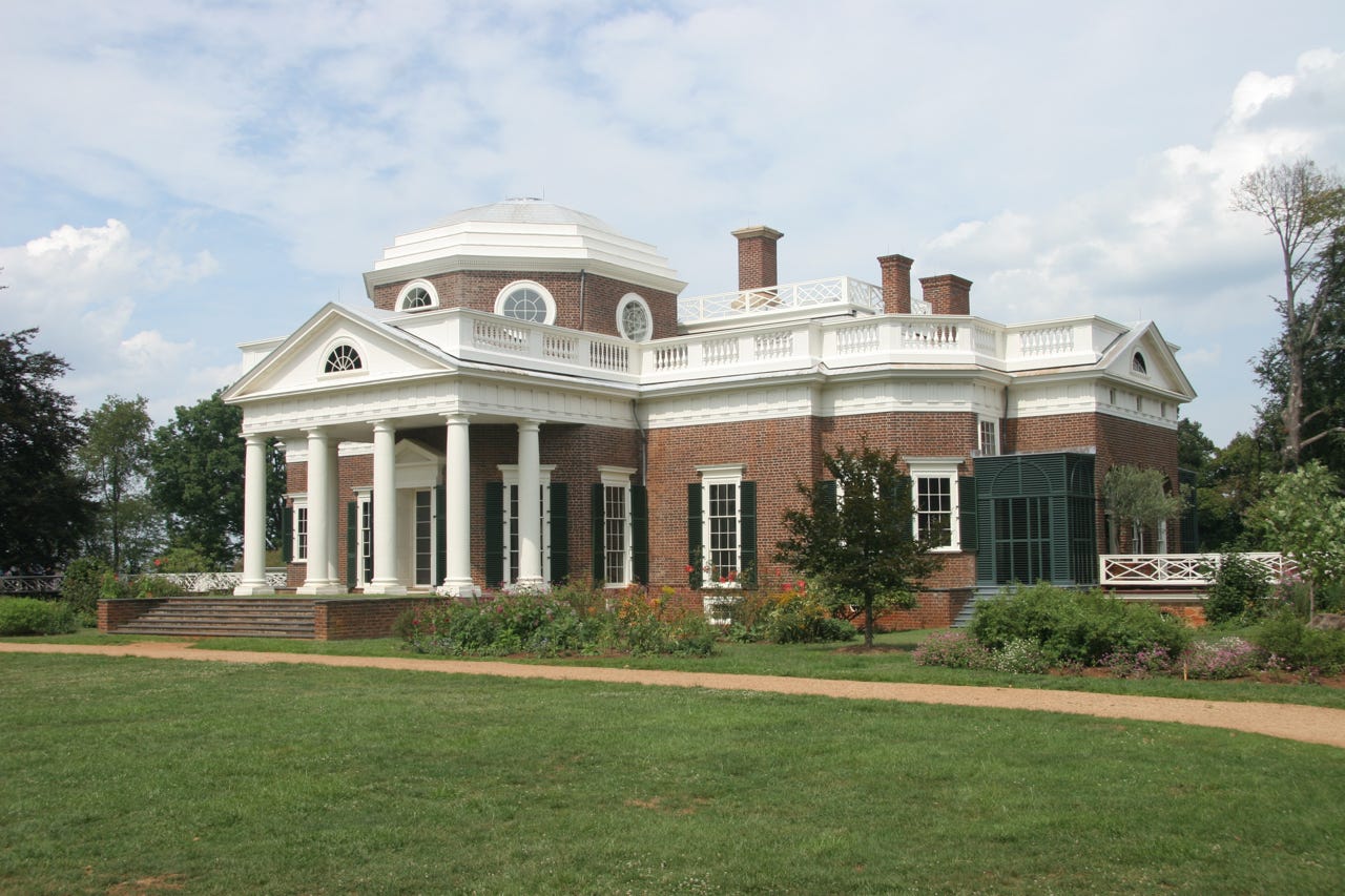 A large brick building with columns with Monticello in the background

Description automatically generated