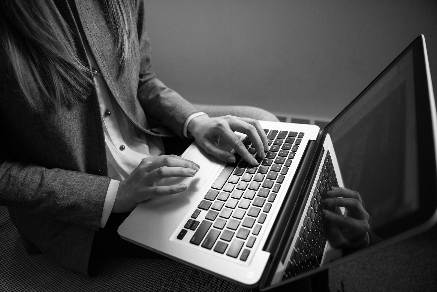 Partial grayscale photo of a woman with a laptop, showing her arms and upper body, with fingers poised over the keyboard