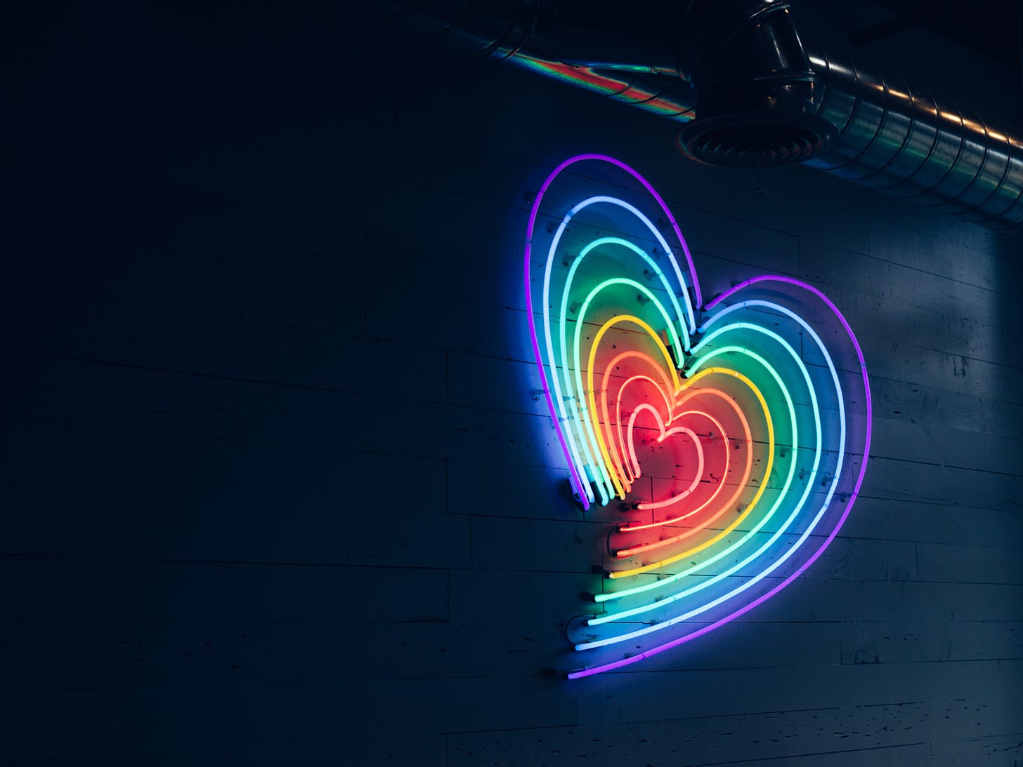 Neon rainbow heart against a black wall