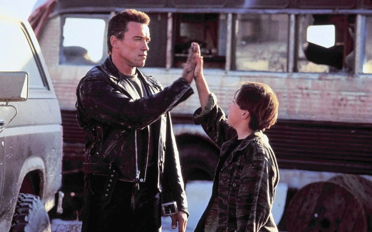 An adult man, played by Arnold Schwarzenegger wearing a black leather jacket, high fives a kid played by Edward Furlong wearing a flannel shirt