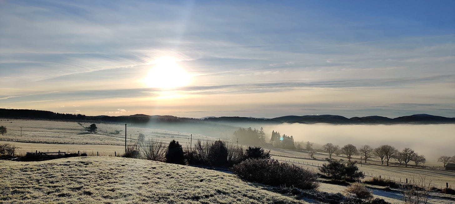 A low winter sun in a blue sky over misty fields in the Scottish Highlands