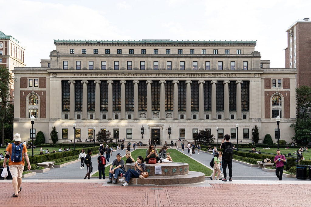 students walking and lounging outside Butler Library, which has pillars across the front and names engraved on the facade