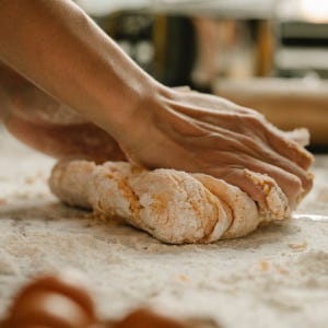 A pair of hands kneading dough on a floured table.