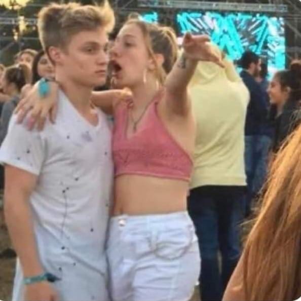 Young woman speaking into young man's ear at concert. Young man seems uninterested.