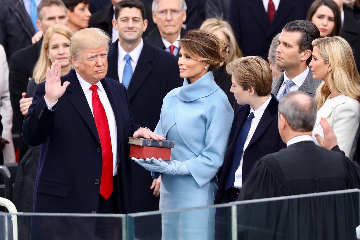 Trump, with his family watching, raises his right hand and places his left hand on the Bible as he takes the oath of office. Roberts stands opposite him administering the oath.