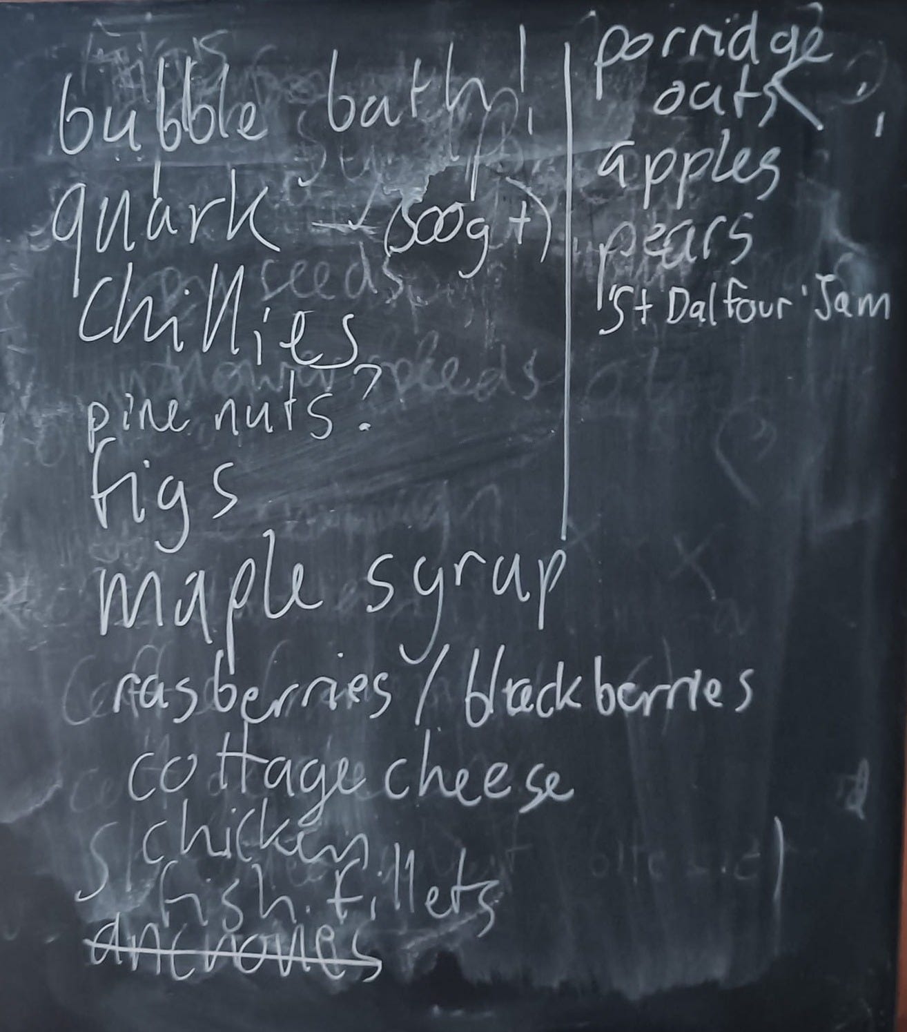 Image is a blackboard with a shopping list scrawled on it: "bubble bath, quark, chillies, pine nute? figs, maple syrup, raspberries / blackberries, cottage cheese, chicken, fish fillets." "Anchovies" is crossed out. It continues: "porridge oats, apples, pears, St Dalfour jam"