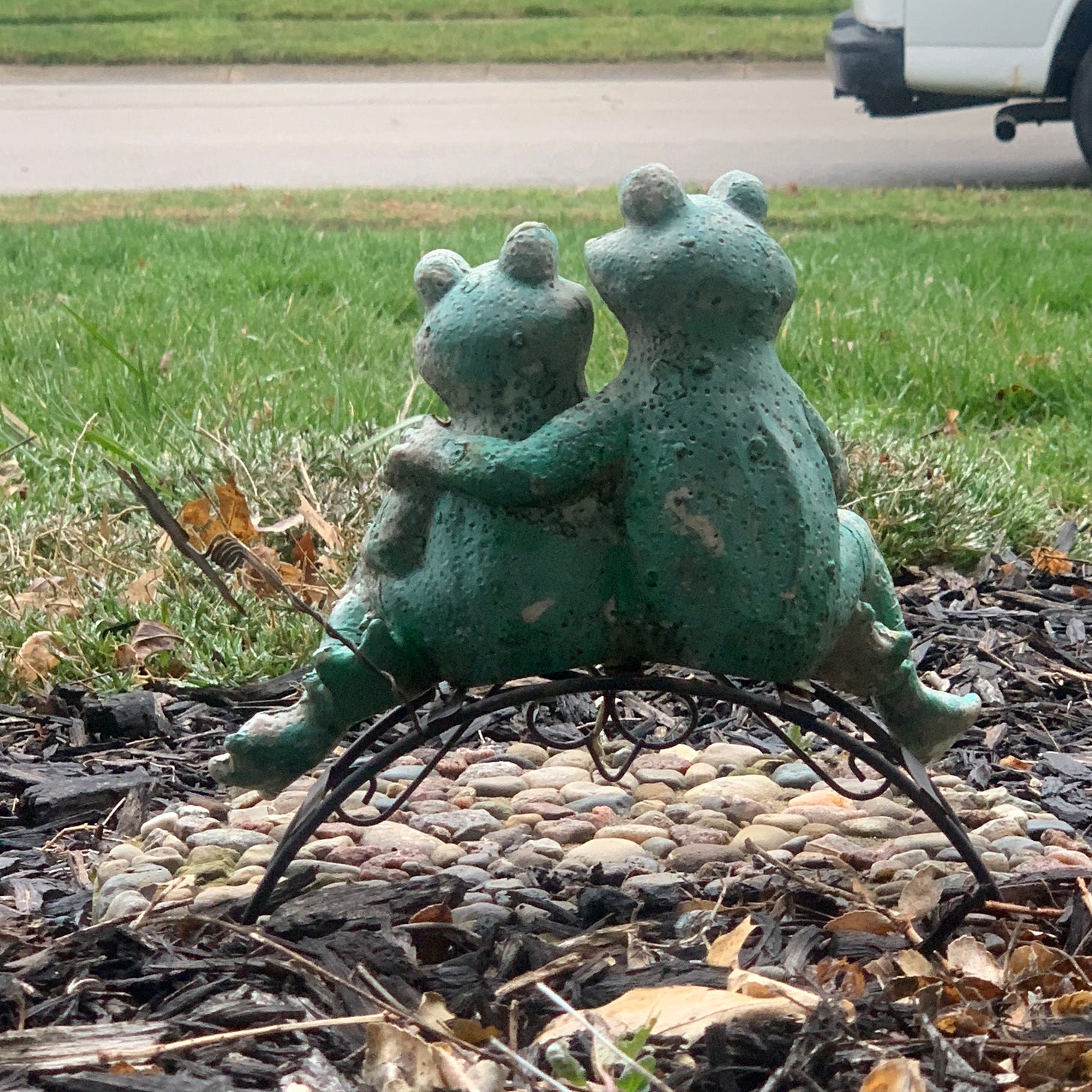 A statue of two frogs sitting beside each other, one with their hand around the other's shoulder