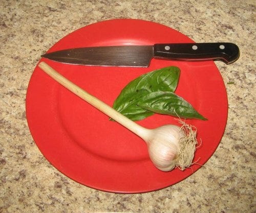 a red plate with a knife, basil leaves, and a garlic bulb