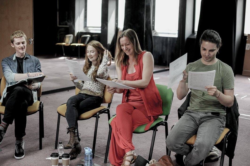 4 actors read from scripts. They are sat on chairs reading, and laughing