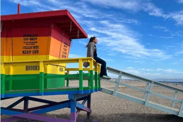 Activist and Army veteran Charlotte Clymer sitting at the beach on a lifeguard dock that is painted rainbow.
