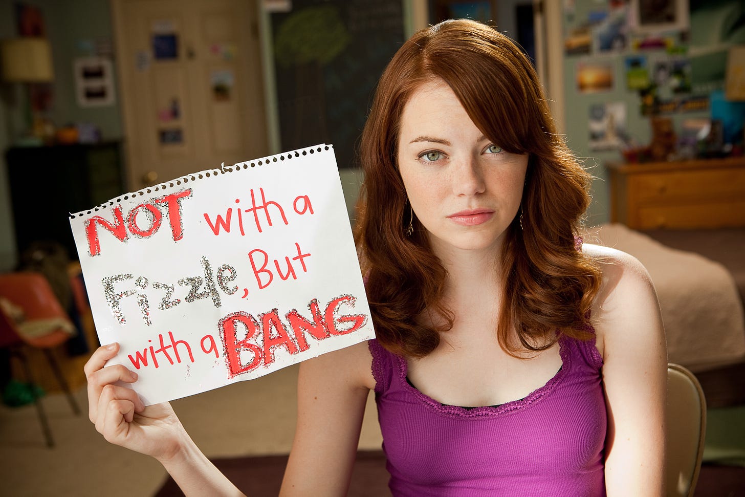 Stone facing the camera, holding a sign that says ‘not with a fizzle but with a bang’