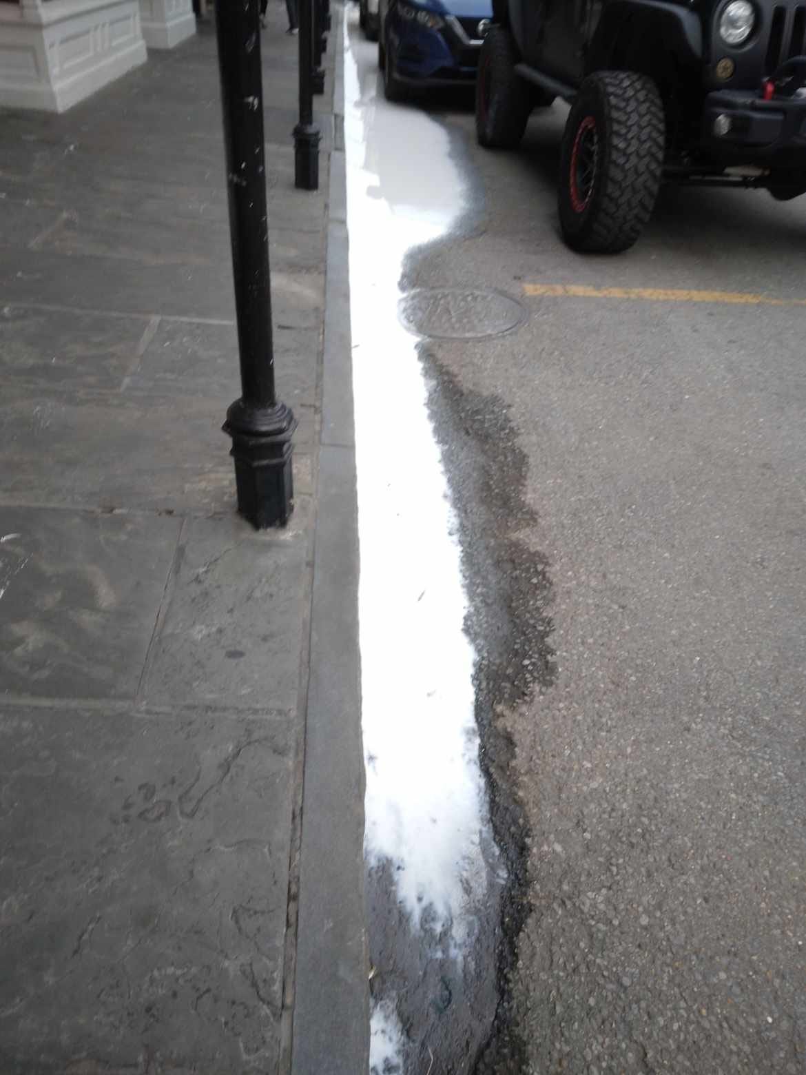Image shows a sidewalk with what appears to be milk in the gutter running beside it.