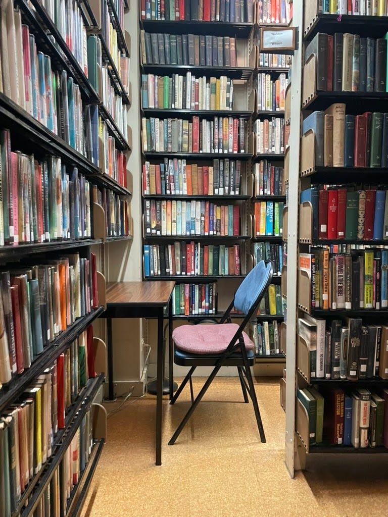 A folding chair and small desk in the stacks of a library