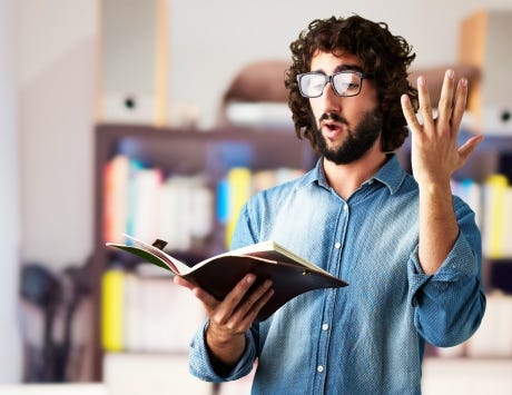 A man in a blue buttoned shirt reading a passage from a book held in his right hand out loud A man in a blue buttoned shirt reading a passage from a book held in his right hand out loud
