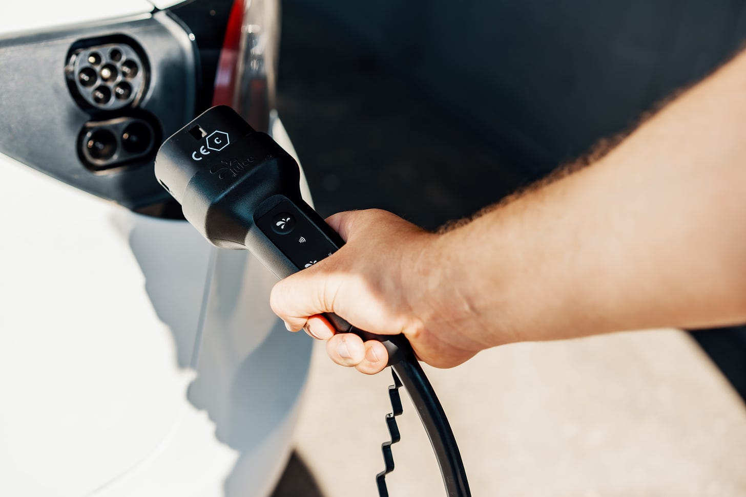An arm holds an electric vehicle charging cable up to a car.