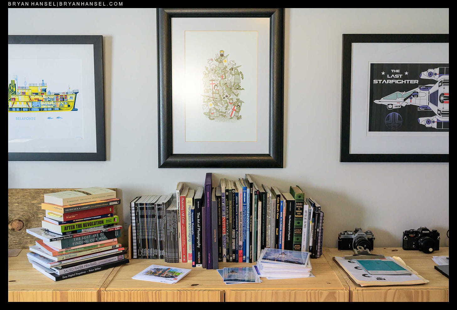 A stack of books next to a stack of books under framed art