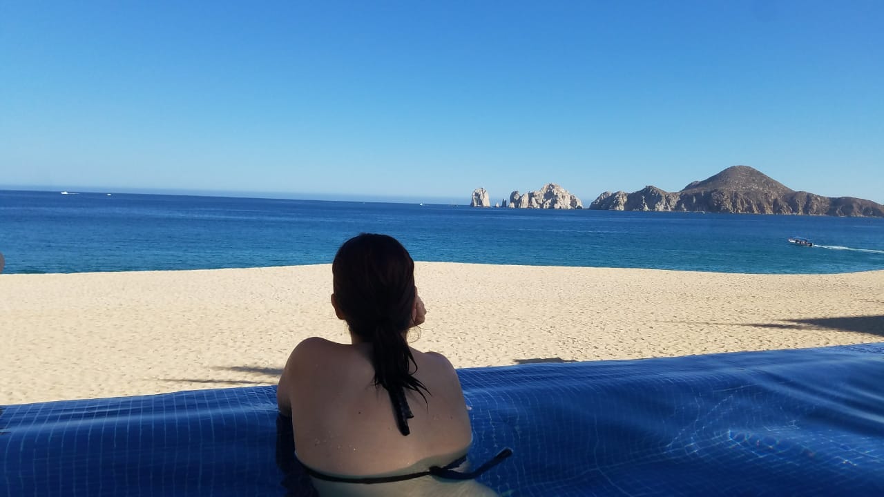 Mujer en una alberca viendo hacia el horizonte en Los Cabos