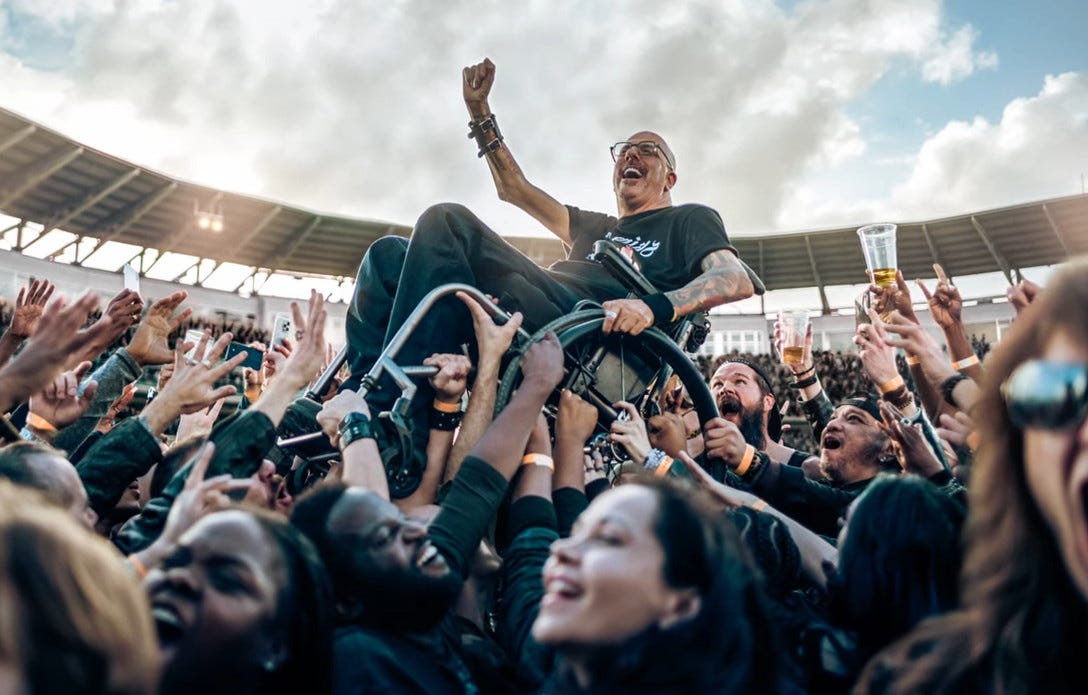 Man in a wheelchair being lifted up by a crowd in an outdoor stadium